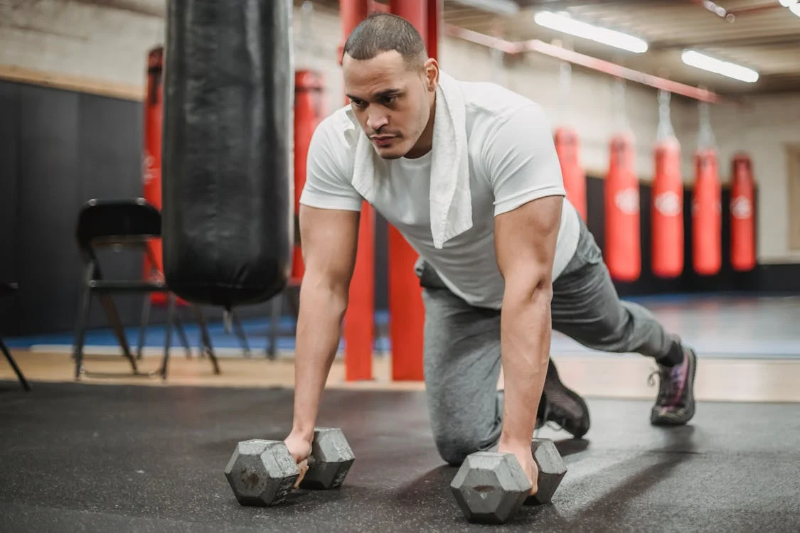 Determined ethnic sportsman doing pushups with dumbbells